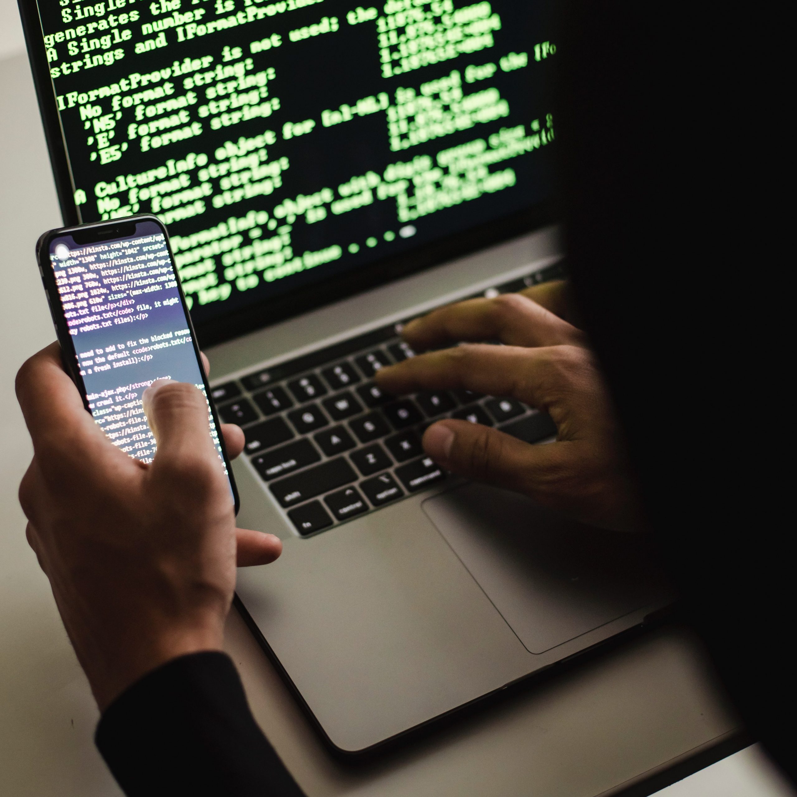 Unrecognizable person using phone to hack computer